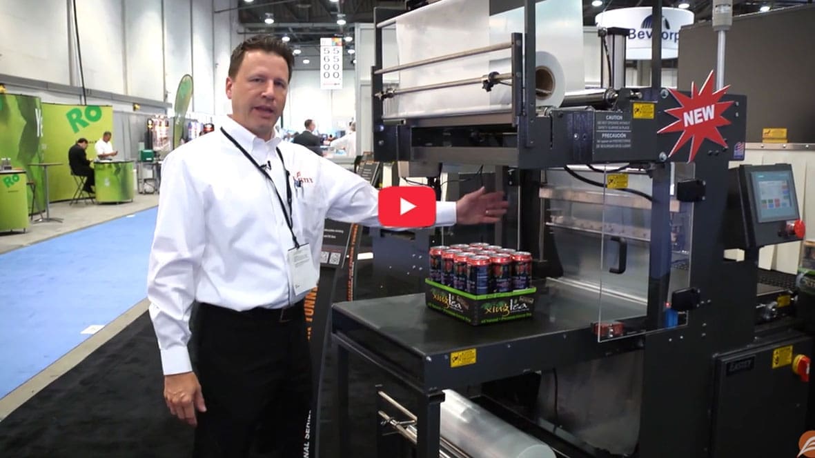 Man showcasing packaging machine at trade show.